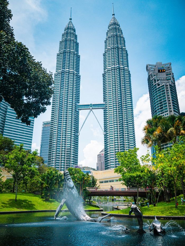 View of Petronas Twin Towers and surrounding park in Kuala Lumpur under a blue sky.