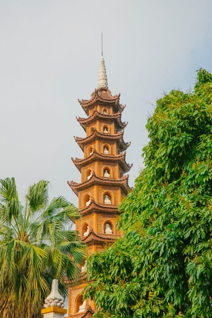 Tran Quoc Pagoda in Hanoi against a clear sky, amidst lush green trees, showcasing Vietnamese architecture.