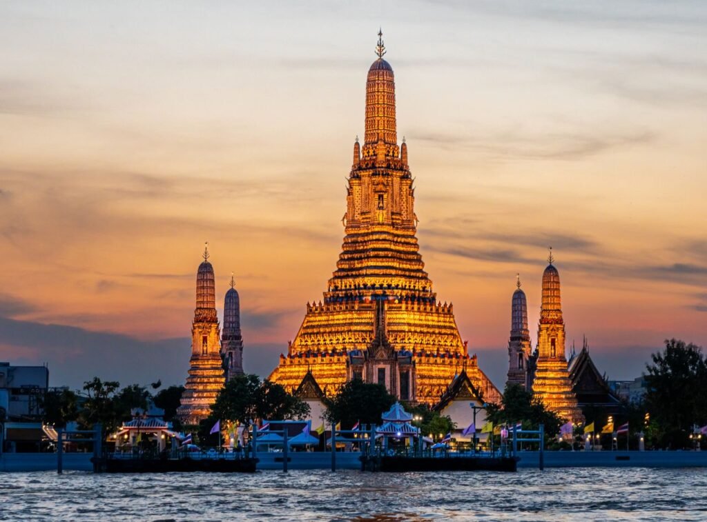 A captivating view of Wat Arun Temple illuminated at sunset along the Bangkok riverside.